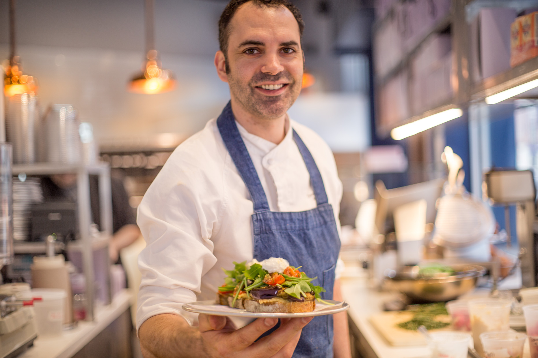 A portrait of Dominique Ansel holding out a plate of food.
